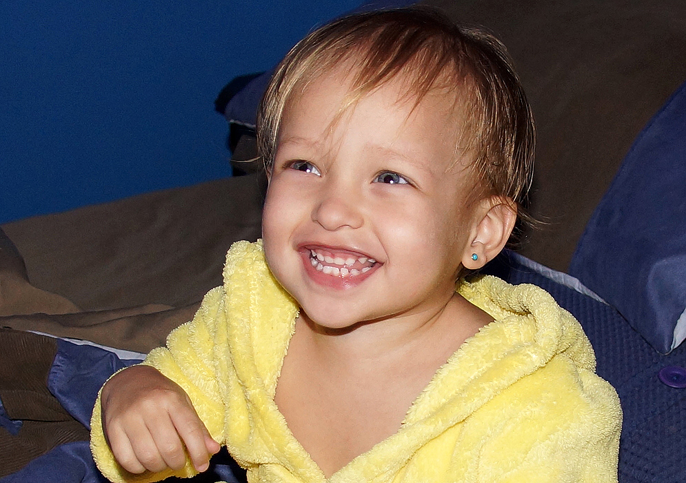 Bebé de 14 meses sentada en la cama con una bata amarilla