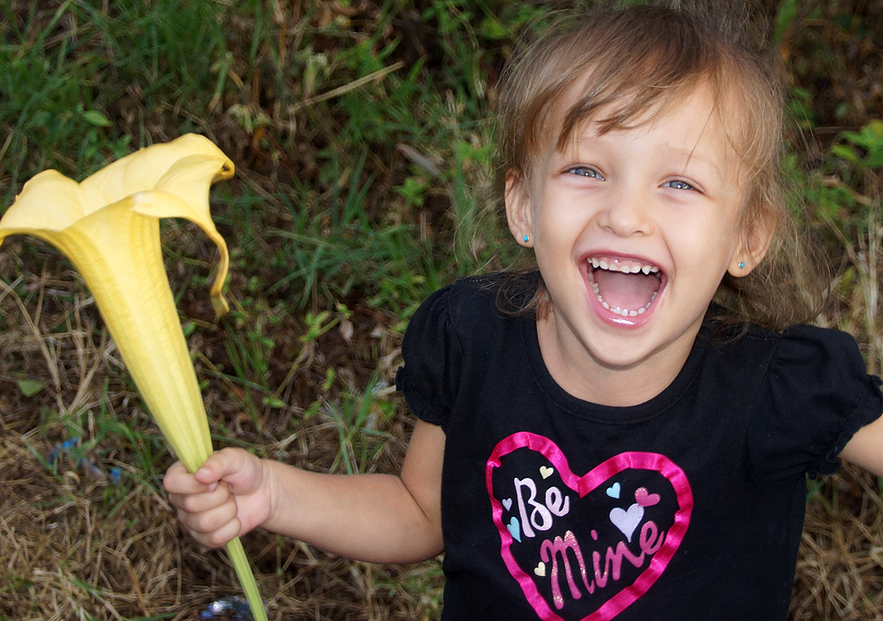 Niña emocionada agarrando una flor amarilla grande