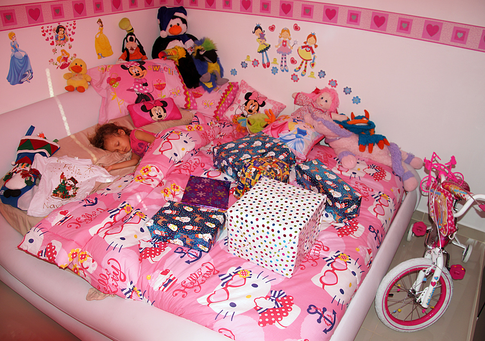 Niña pequeña durmiendo en una cama grande llena de regalos en la mañana de navidad